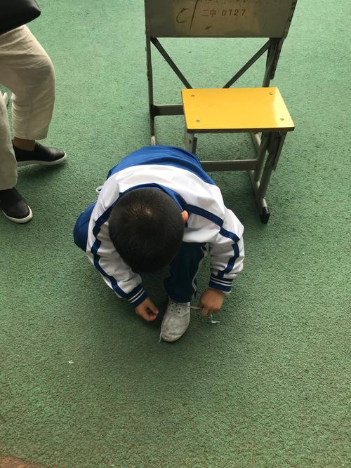 4岁小男孩蹲在走廊用磁铁碰校服拉链的真实抓拍