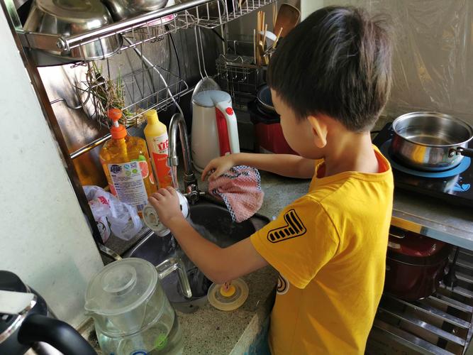 小男孩踩矮凳在厨房帮妈妈擦灶台的真实抓拍