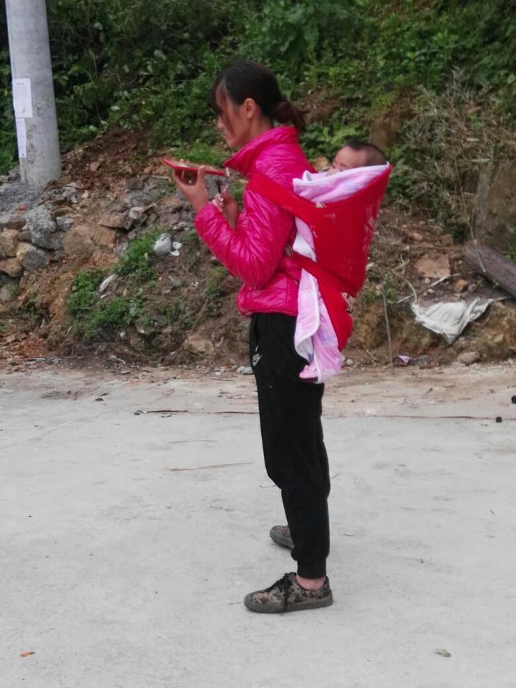 苗族母亲用传统背带背着孩子在山间劳作
