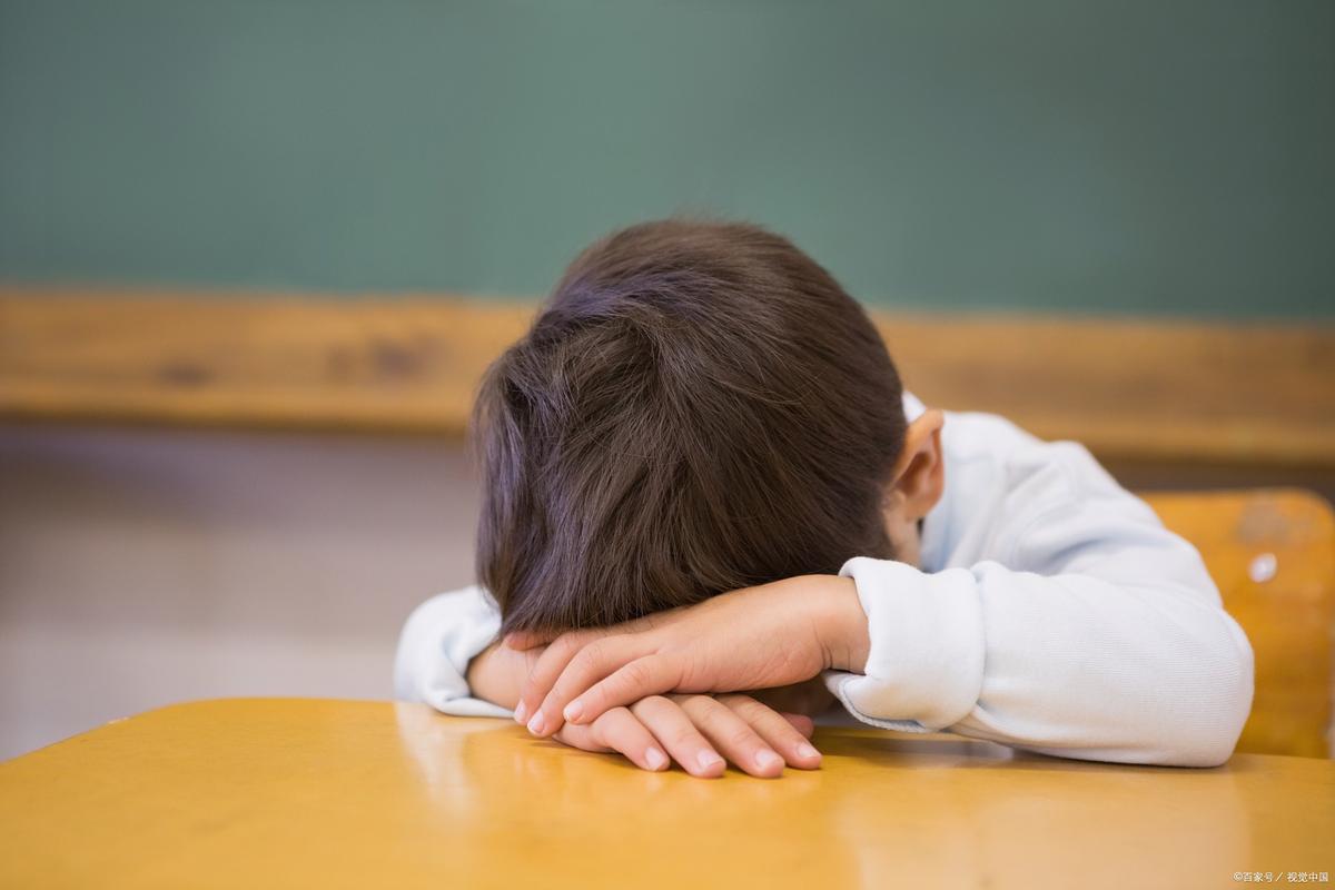 六岁儿童刚上小学趴在桌面情绪低落场景图