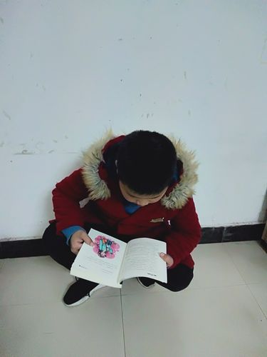 小学低年级孩子蹲在绘本架旁专注读故事书的实拍图