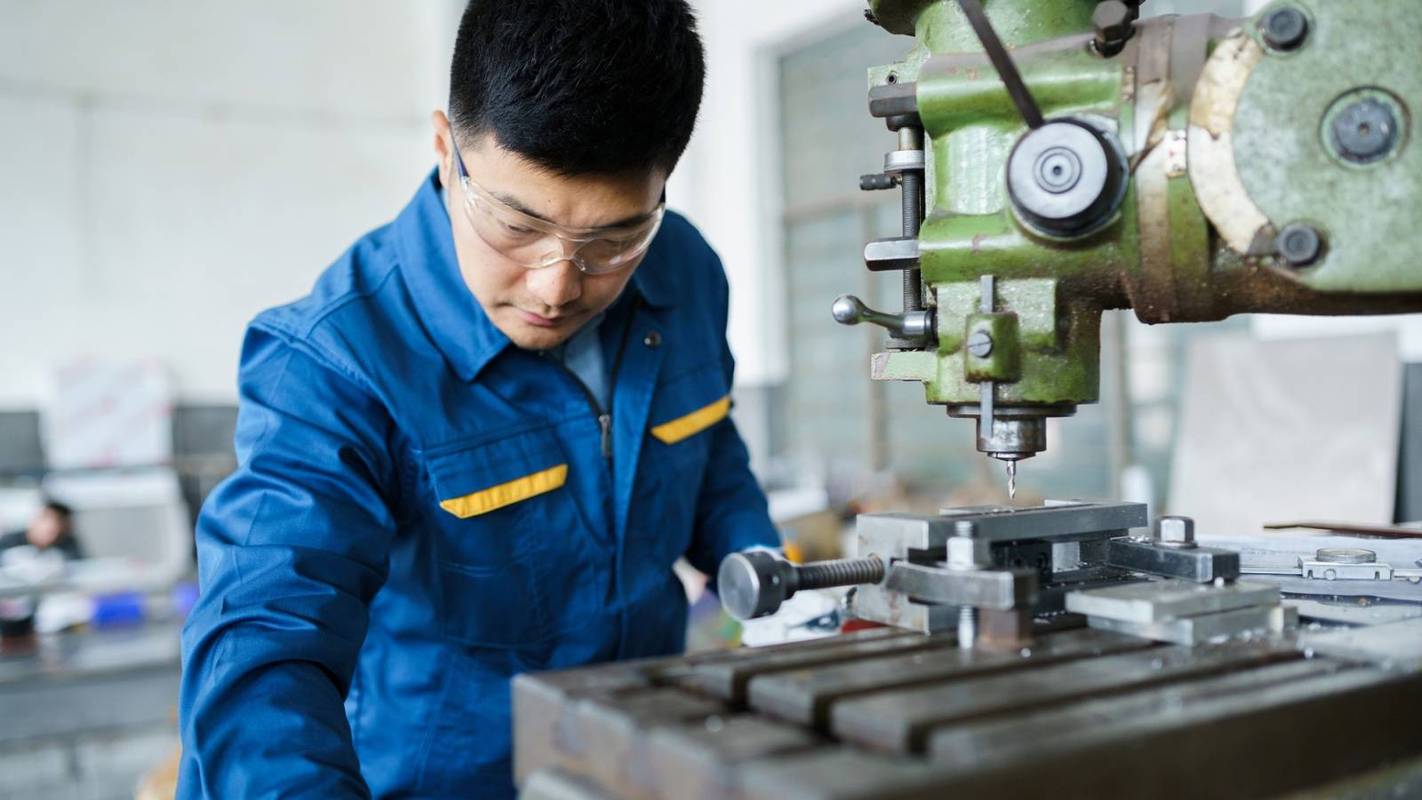 机械加工车间老工艺师对着图纸给年轻工程师讲解的现场照片