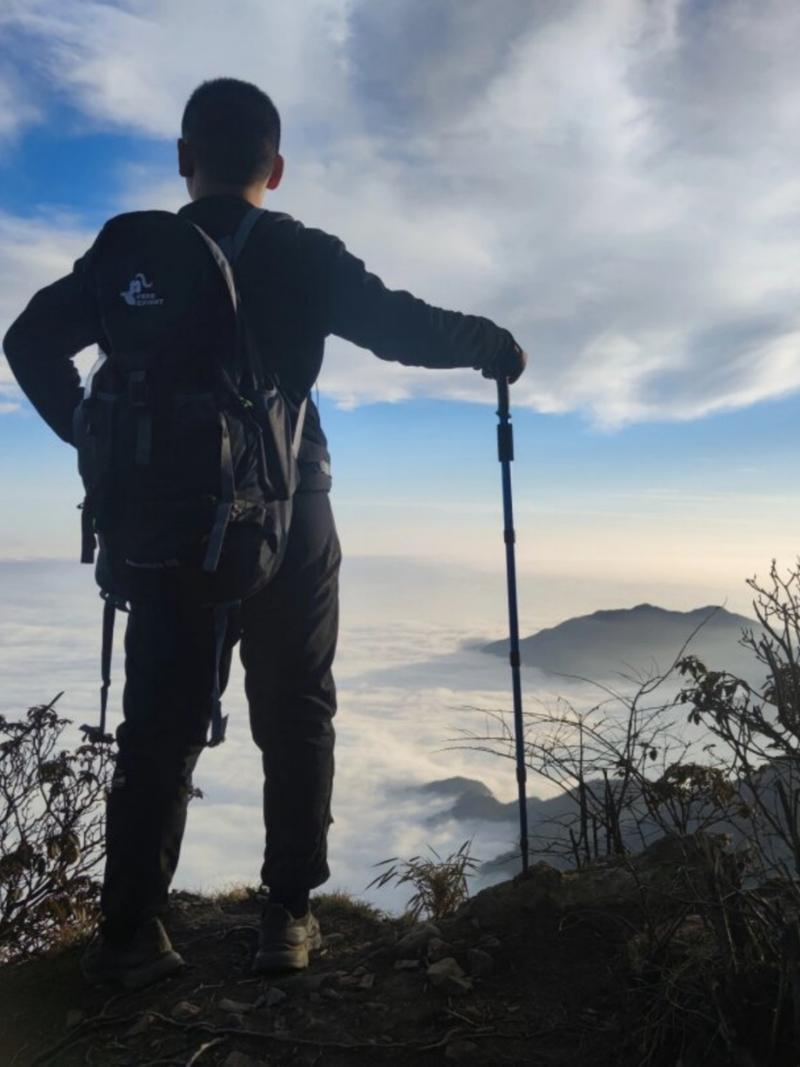 登山者手持双杖在崎岖山路行走背影