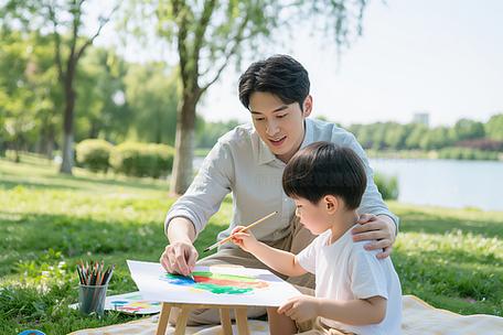 周末公园父子坐草坪一起画画温馨场景