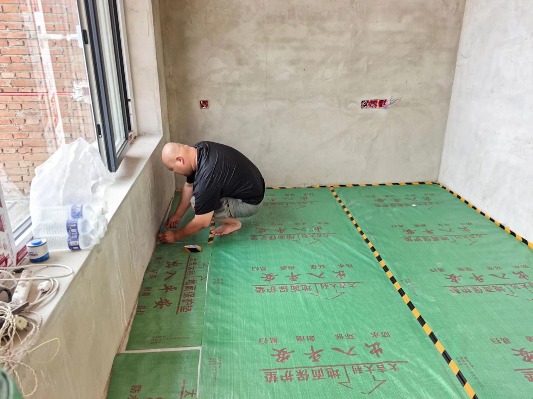 装修工人铺设木地板前在地面铺防潮膜的过程
