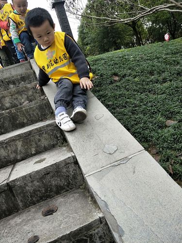 小男孩蹲在小区滑梯台阶上踢石子皱眉头