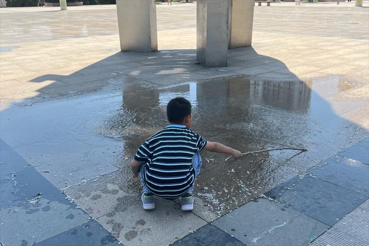 小男孩蹲在地上观察水坑倒影特写