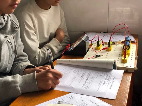 中学物理老师蹲在课桌旁给学生讲电路题的实拍图