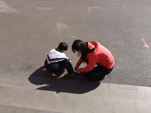 小学走廊上两个小孩蹲身系鞋带的背影