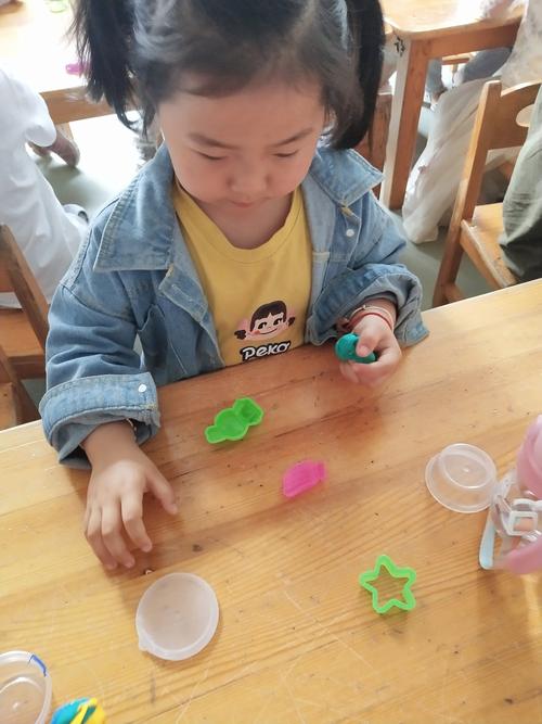 幼儿园小朋友蹲在小区台阶上捏彩泥观察材质的实拍图