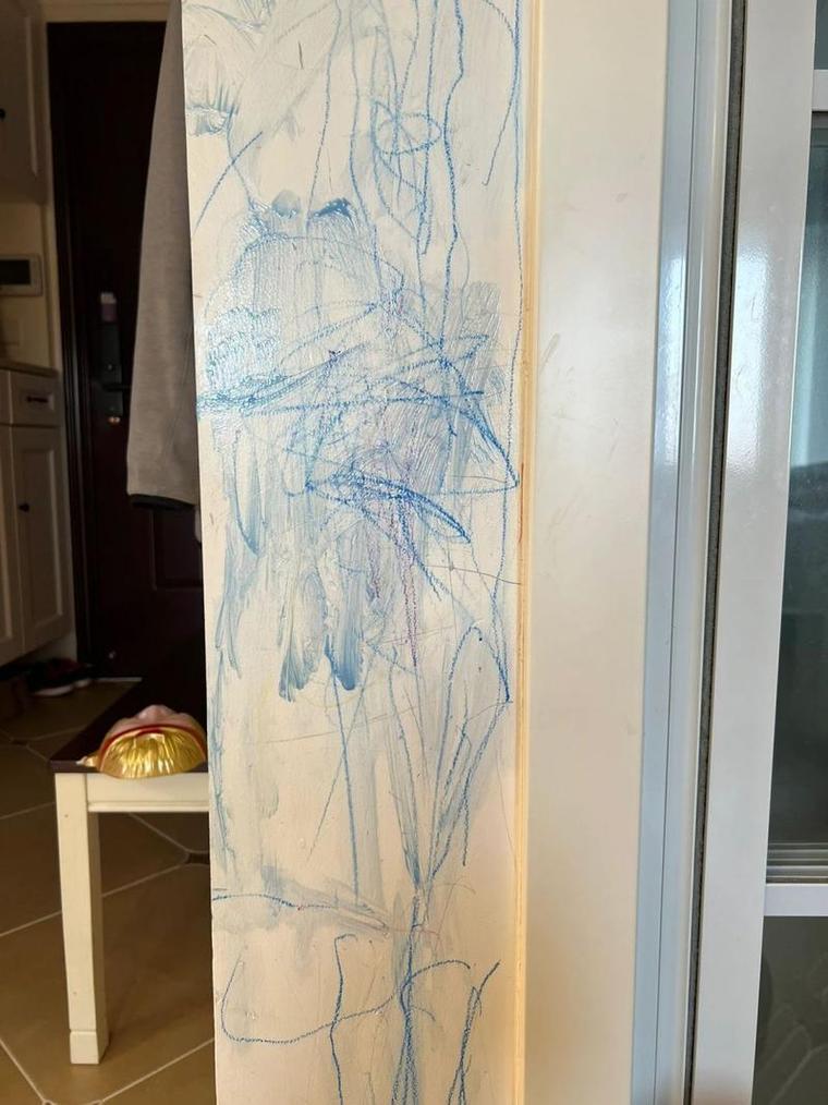 3岁幼儿举着蜡笔面对被涂花的白墙表情紧张