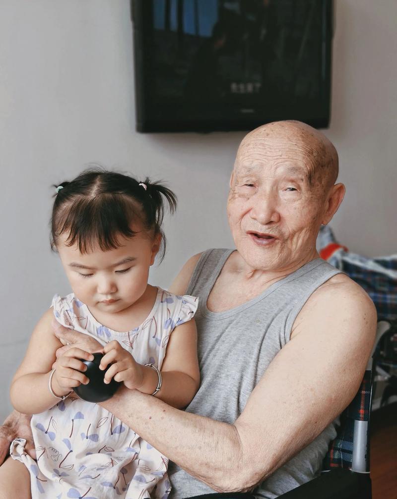 爷爷抱着2岁幼儿坐在布艺沙发上讲方言老故事的日常场景