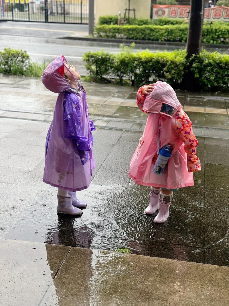 孩子在雨中穿着雨衣快乐踩水坑，妈妈在旁边微笑看着