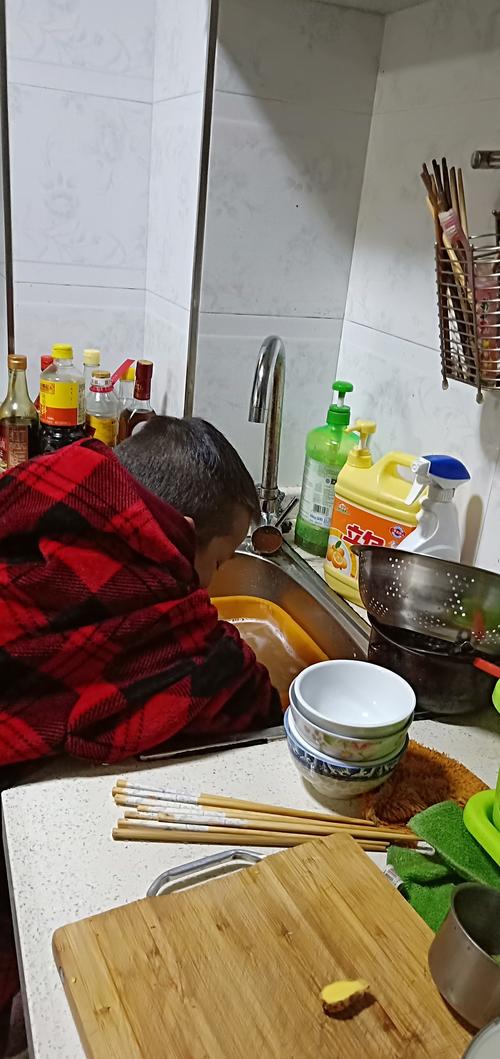 小孩踩着小板凳在水槽边洗碗的侧影