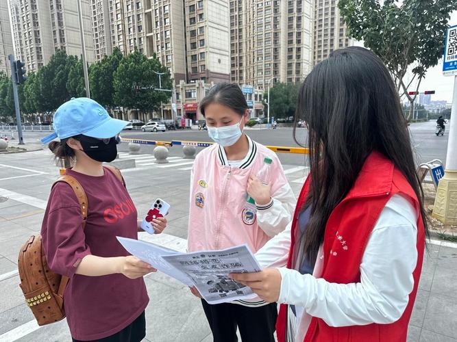 社区反诈摊位穿红马甲的年轻志愿者发传单