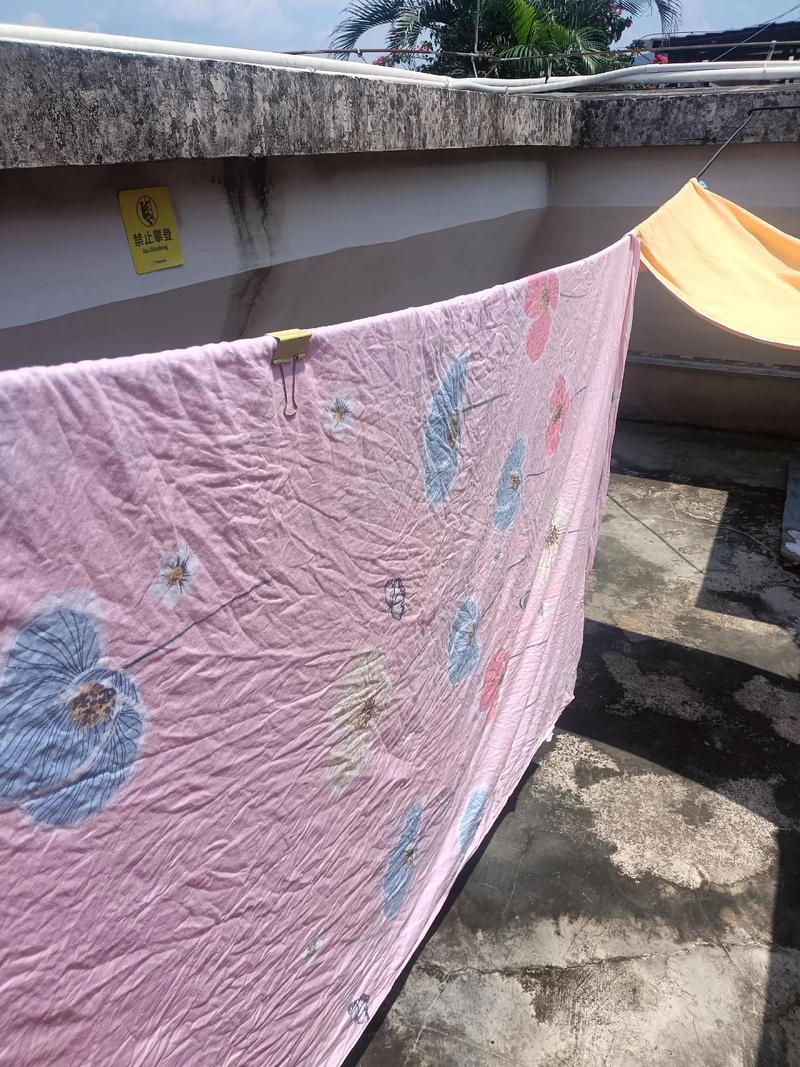 居民楼下单元门旁晒着的厚乳胶床垫沾樟树果印