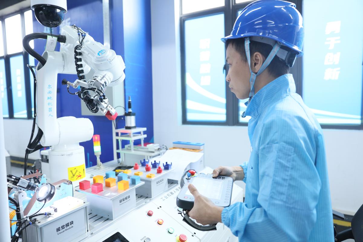 车间工人手持工业机器人示教器操作图