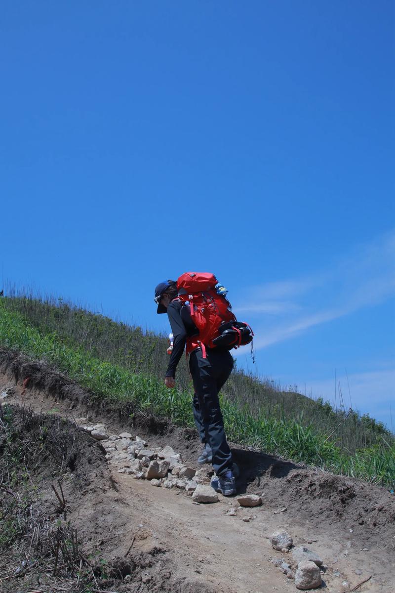 登山者背负行囊在陡峭山路稳步向上目光坚定