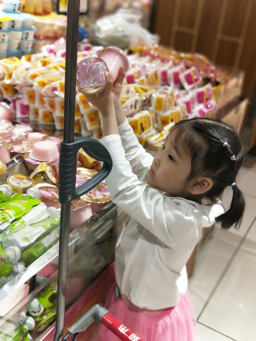 5岁小女孩蹲在便利店冰柜前盯着瓶装橙味汽水发呆