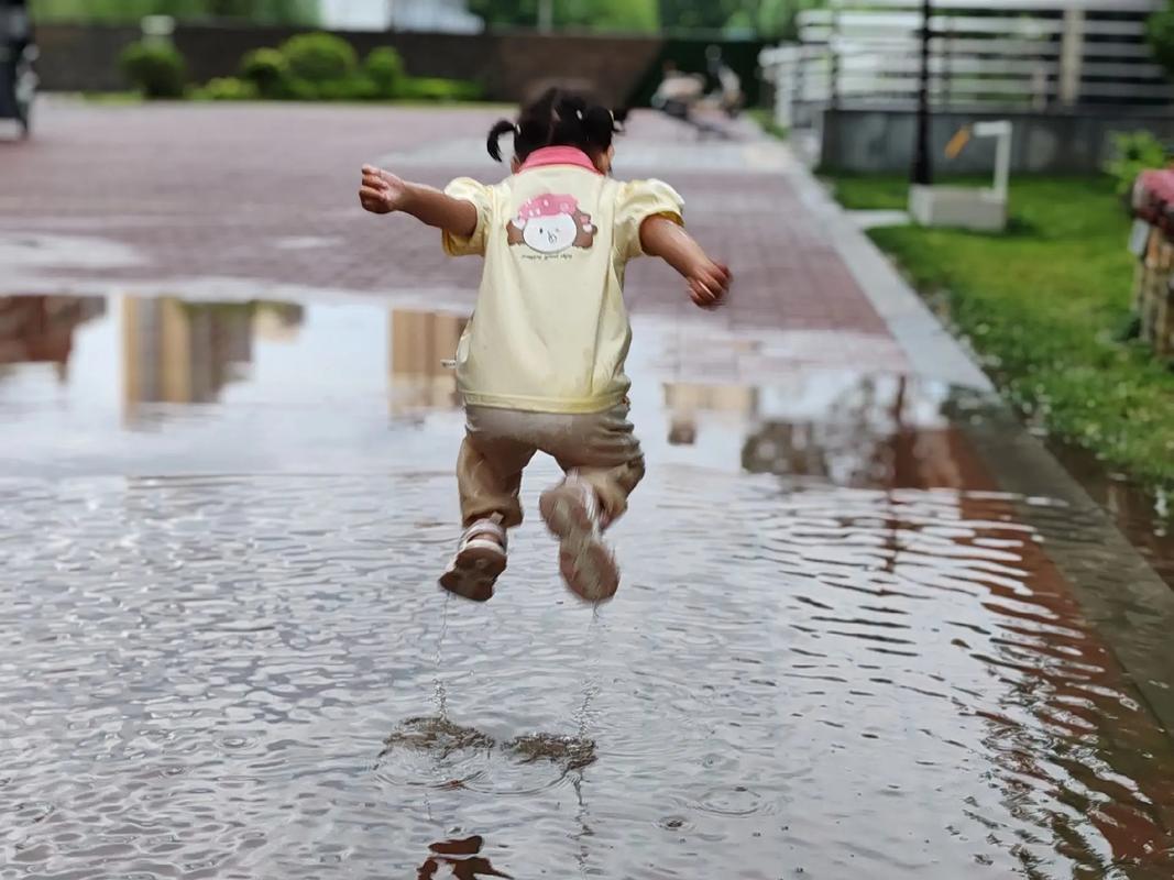 儿童蹲在地上观察雨后水洼倒映的天空