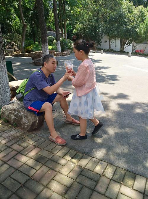 小区花坛边两个小学生面对面拌嘴举着半块冰棒的日常场景