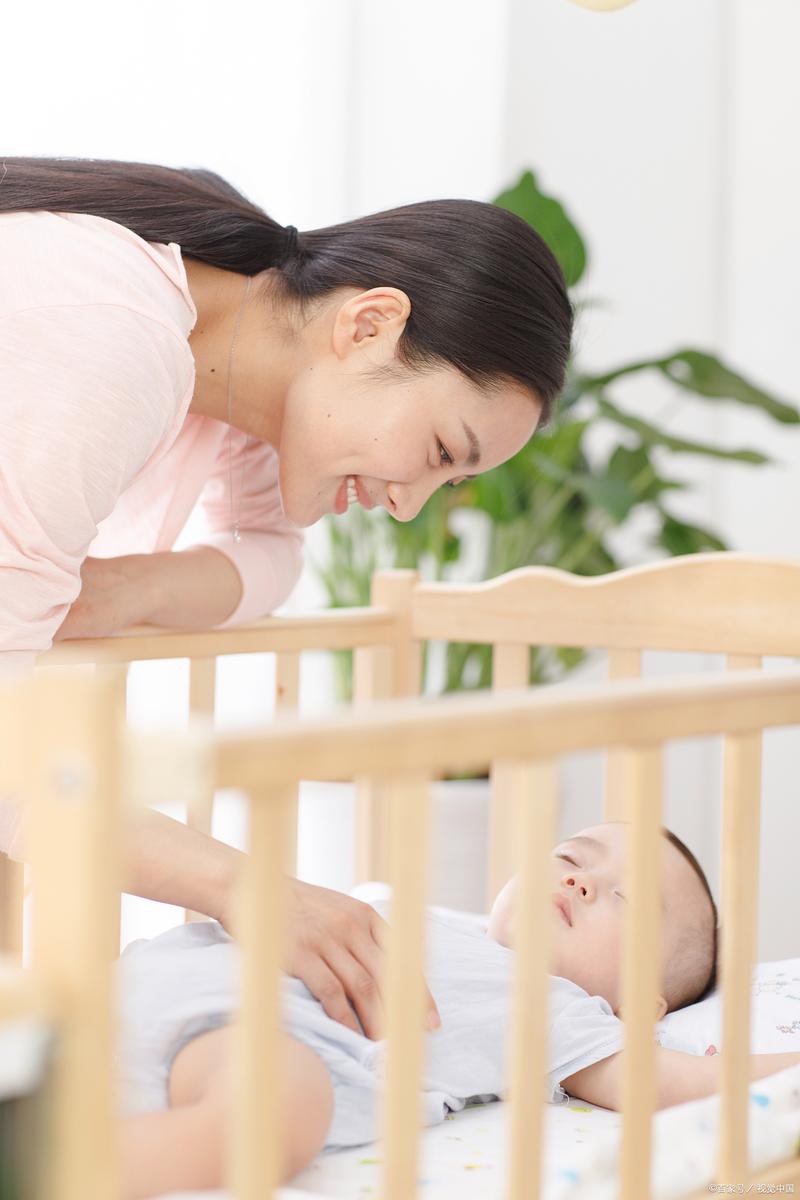 妈妈蹲在婴儿床边轻拍婴儿胸部安抚宝宝入睡