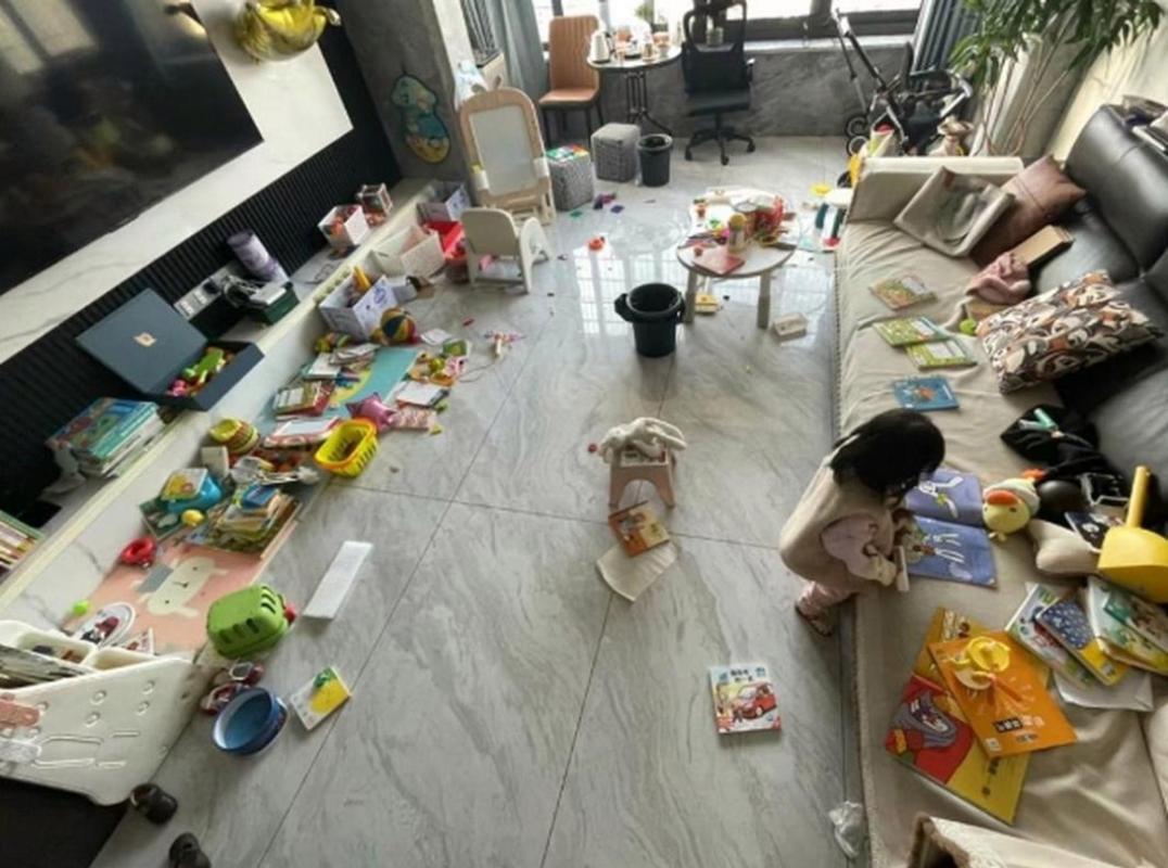 爸爸在乱糟糟的客厅里无奈地给撕书的小孩收拾残局