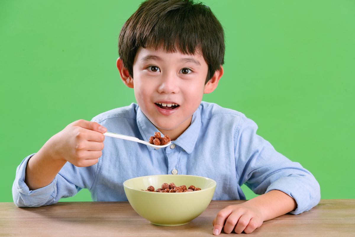 2岁幼儿坐在餐椅上自己拿勺子舀饭的实拍