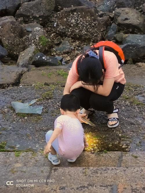 妈妈蹲在旁边看小孩蹲地上踩水洼的日常场景