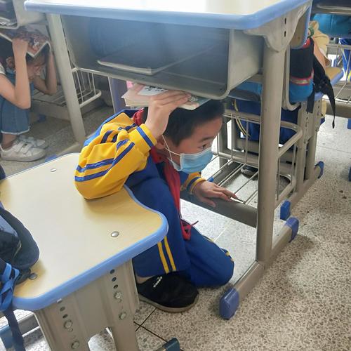 小学低年级学生蹲在课桌边哄摔在地上的铅笔盒