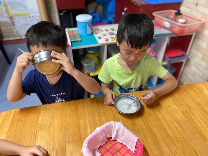 两个小男孩坐在餐桌旁用筷子和纸杯做简易天平放硬币的实拍图
