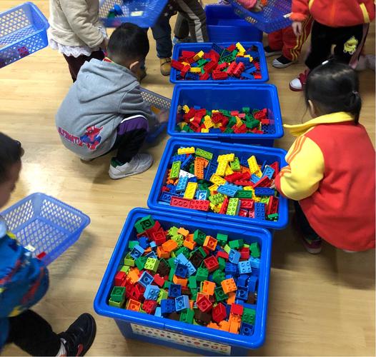 2岁幼儿整理社区儿童游乐区散落积木的实拍图