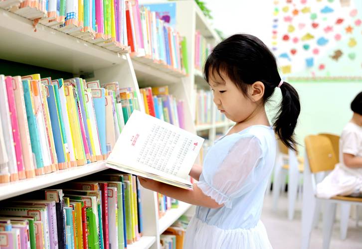 小学生独自在图书馆捧着厚书阅读