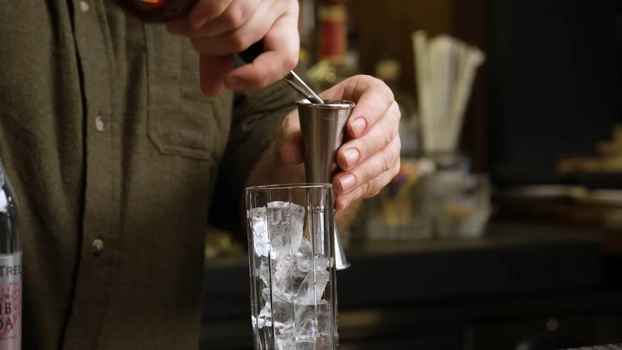 调酒师夹取透明老冰放入威士忌杯的特写