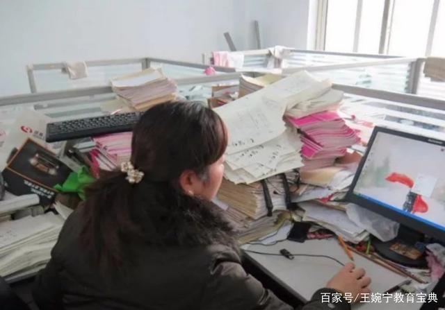教师在杂乱办公桌上对比纸质成绩单和电脑数据图表