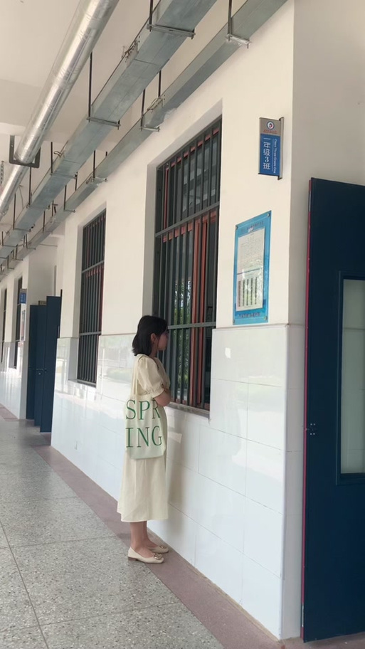 小学教学楼走廊靠窗捏润喉糖的女老师侧影