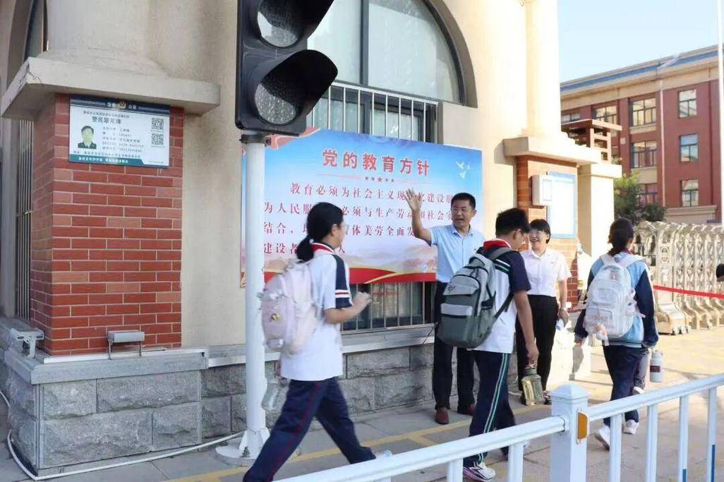 中学校长身着正装站在学校正门迎接学生进校的真实场景