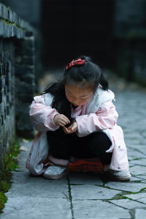 妈妈蹲在学校门口平视手里攥着皱手工纸的小女孩
